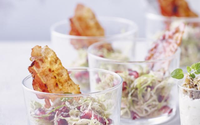 Glaasjes met spruitjessalade, gelakte spekreepjes en granaatappeldressing