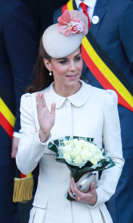 In een crĂšmekleurige mantel van Alexander McQueen met hoed van Jane Taylor, oorbellen van Kiki McDonough en clutch van Alexander McQueen