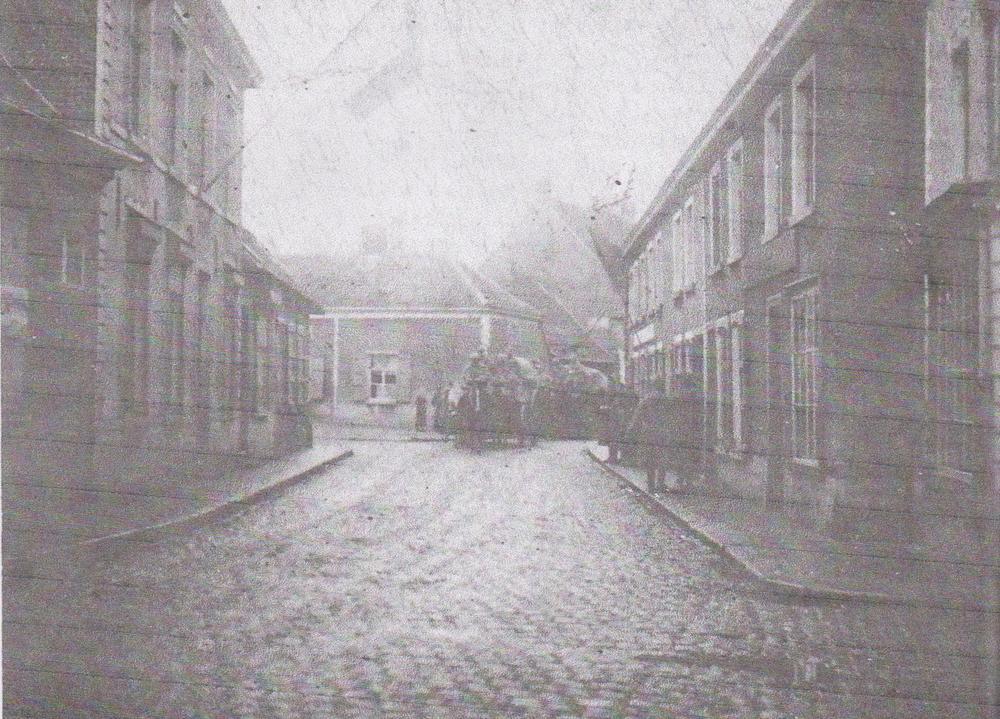 De intocht van Franse soldaten in de Bruggestraat op 19 oktober 1918, het kruispunt Bruggestraat-Oude Tieltstraat. In de achtergrond doemen legerwagens op, door paarden getrokken. Rechts staan militairen, links kijken burgers toe. In het grote huis met Belgische vlag woonde drankverkoper Henri Verhalle-Schacht. Het laatste huis links was van kleermaker Arthur Castelein, later Elektro Van Cauwenberghe en nu een appartement. In het zijstraatje vooraan rechts was er een Duitse veldkeuken. Ook burgers stonden er soms in de rij met hun 'kortwagen' om met een bon een rantsoentje af te halen bij handelaar in kolen Emiel Goossens-Van Poucke.