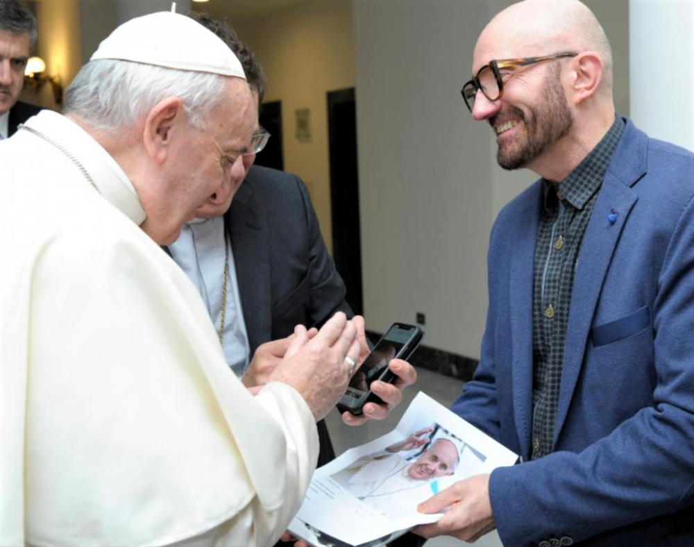 De paus bekijkt op de smartphone van Mgr. Aerts een beeld van moeder Berten die wuift vanuit het ziekenhuis; rechts broer Patrick.