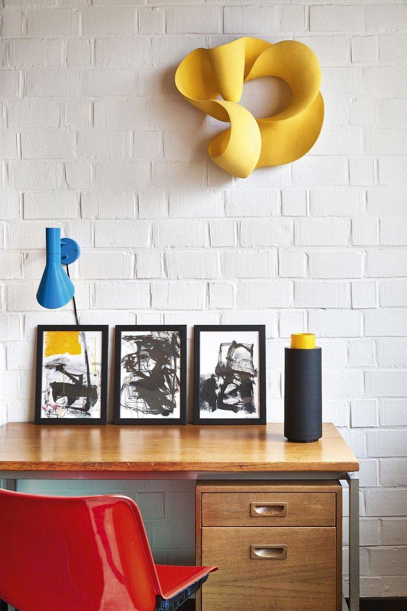 De bureauhoek met rode vintage bureaustoel van Tecno. De lamp is van Arne Jacobsen, de grafiek van Anastasio Marquez, de vaas van Anna Torfs. Aan de muur hangt de gele oneindige wandsculptuur van Merete Rasmussen, geïnspireerd op de ring van Möbius.