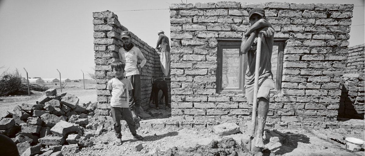 Een paar jonge mannen bouwen een gelijkvloers huis voor Aydan (58) in een opvangkamp. De man bleef aan als schoolhoofd tijdens de bezetting van ISIS en werd daarvoor veroordeeld, maar is nog steeds bang voor vervolging.