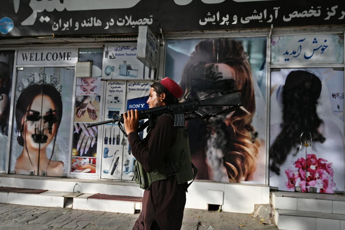 Een talibanstrijder stapt voorbij uitgeveegde foto's van vrouwen in Kaboel, 18 augustus 2021 