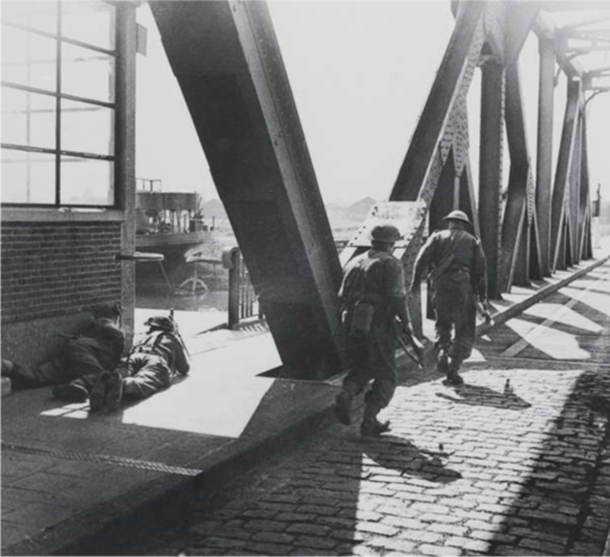De strijd aan de haven: twee Britse soldaten zoeken dekking, terwijl anderen de brug oversteken om nieuwe posities in te nemen in de Antwerpse dokken.