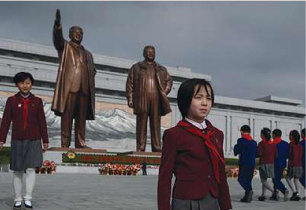 Noord-Koreaanse schoolkinderen leggen bloemen bij de standbeelden van Kim II Sung en Kim Jong II. 