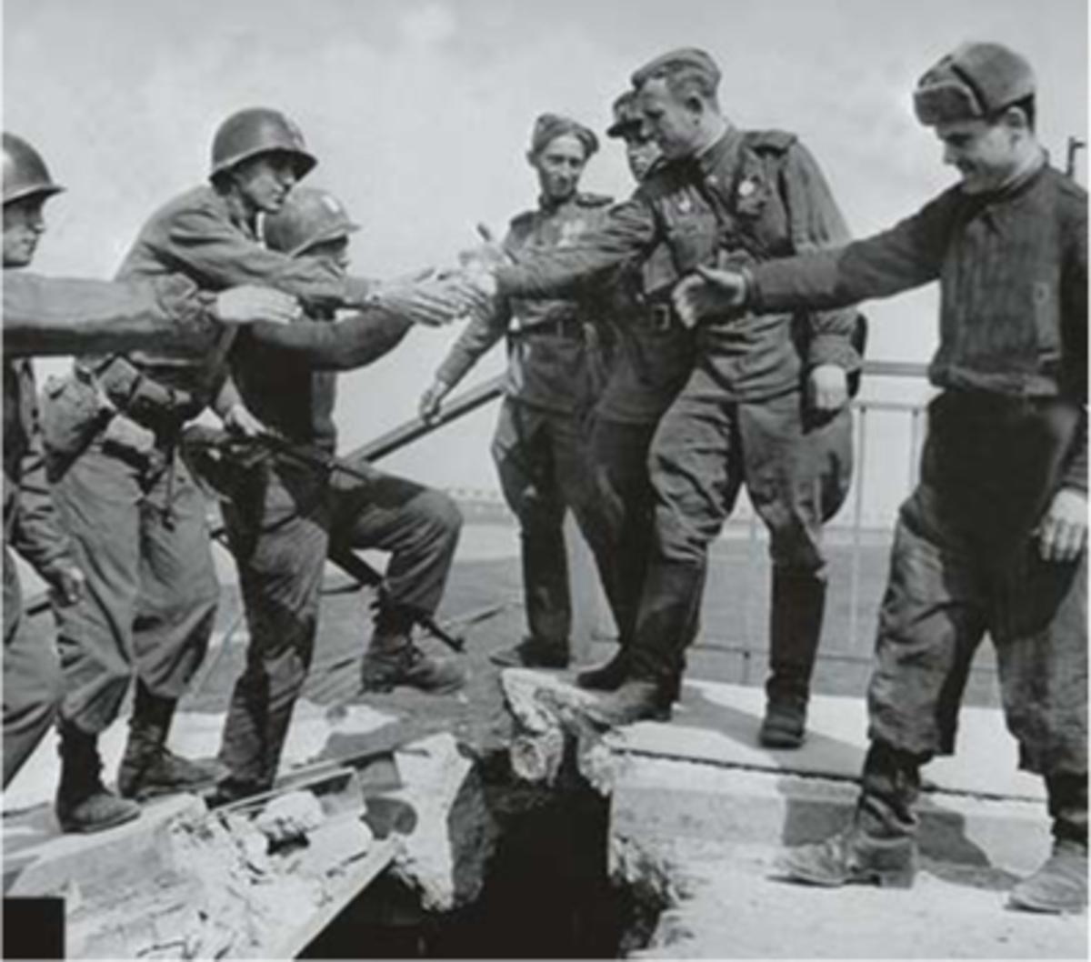 Duitsland, 27 april 1945: Russische en Noord-Amerikaanse troepen ontmoeten elkaar in Torgau bij een vernietigde spoorbrug over de Elbe. Generaal F.A. Reinhardt, aanvoerder van de 69ste Amerikaanse infanterie-divisie, schudt de hand van een onbekende Sovjet-generaal van de Russische Garde.