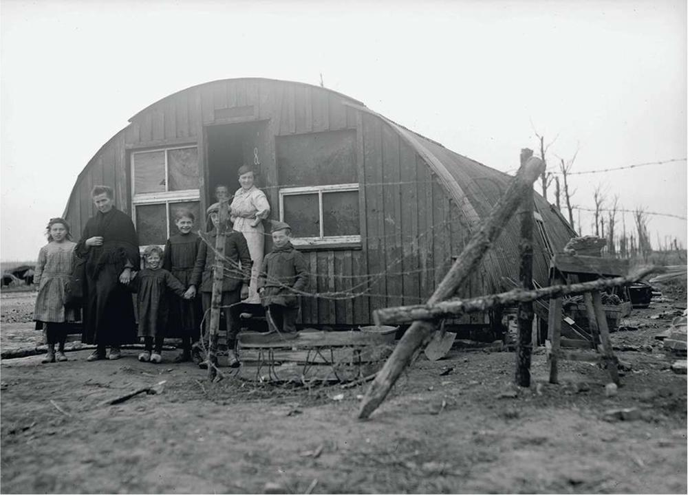 Een familie van teruggekeerde vluchtelingen voor de ingang van een Britse legerbarak (Nissen Hut) in Geluvelt.