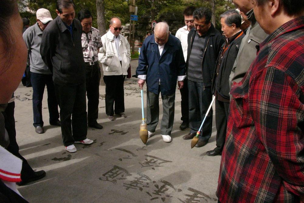 Peking, Chaoyang park: een oude man tekent oude Chinese karakter met water op de grond. Toeloop van jongeren die die karakter vergaten. Onbewust passief verzet tegen het nieuwe China dat hen opgedrongen wordt?