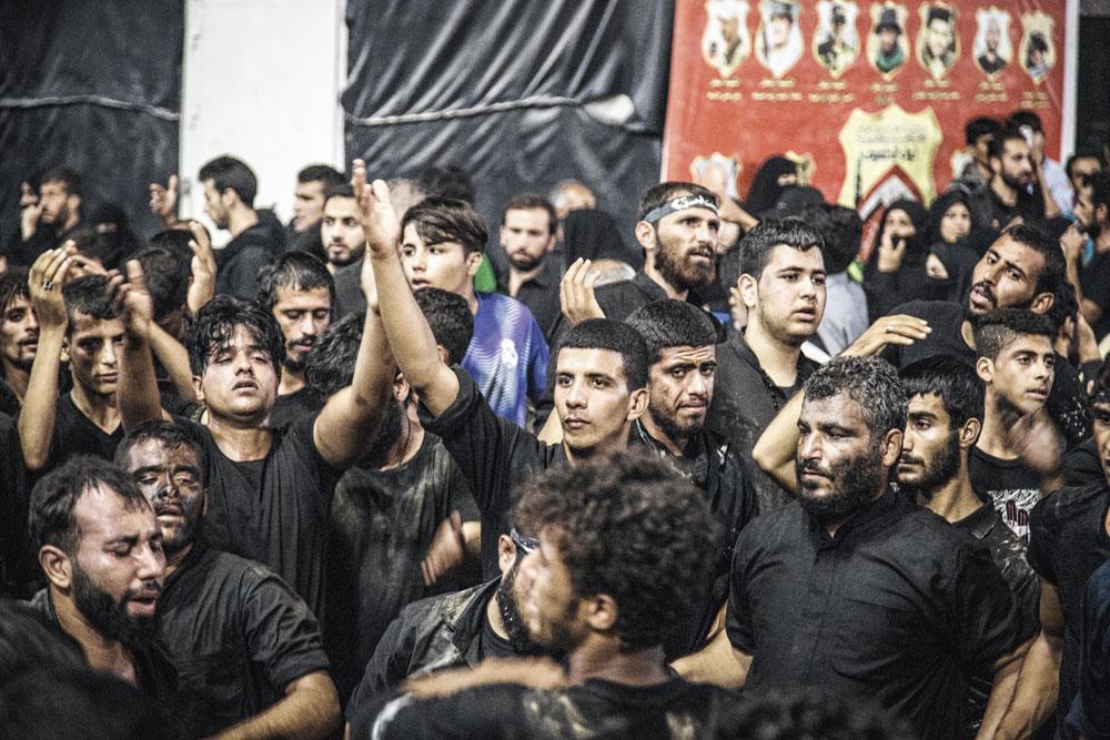 Jonge Iraakse mannen, sommigen met modder op hun kleren, slaan hun handen tegen het hoofd en de schouders als teken: 'Hoessein, we zijn er'.