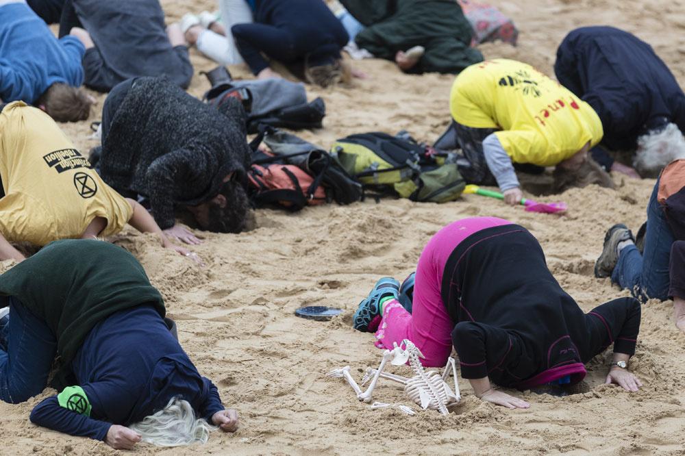 Activisten van Extinction Rebellion steken hun kop in het zand op een strand in Sydney om aandacht te vragen voor de klimaatcrisis.
