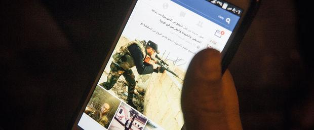 Een syrische vluchteling laat verschillende facebook-foto's zien van voormalige syrische militieleden.