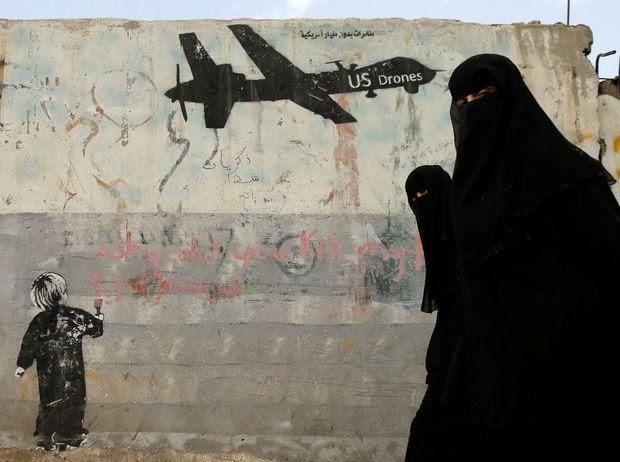 Twee vrouwen wandelen voorbij een muurschildering in de Jemenitische hoofdstad Sanaa die Amerikaanse drones aan de kaak stelt 
