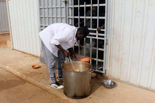 Een man geeft migranten eten in een van de detentiekampen nabij Tripoli in Libië