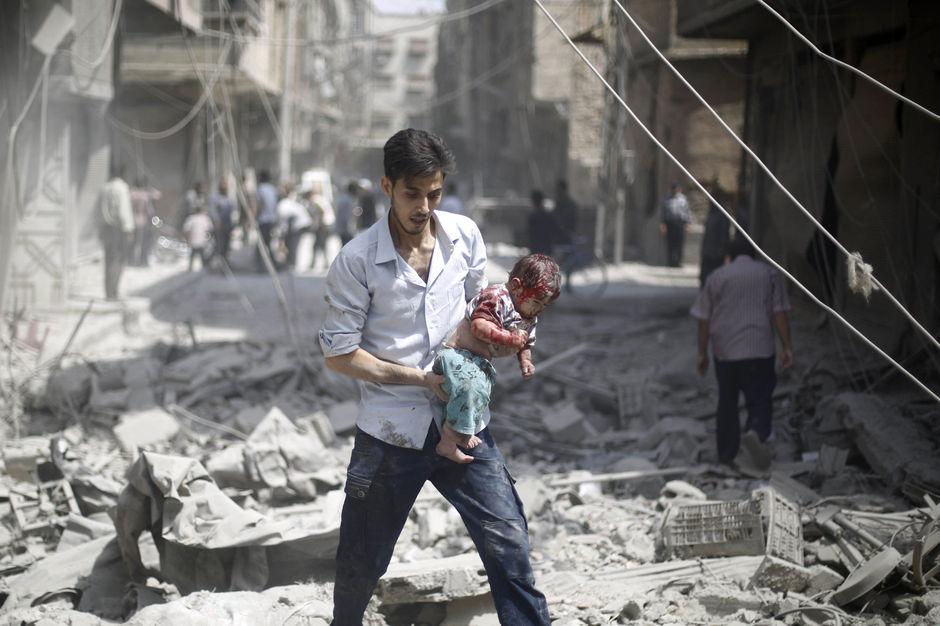 Een man draagt zijn kind in de gebombardeerde stad Douma, niet ver van Damascus