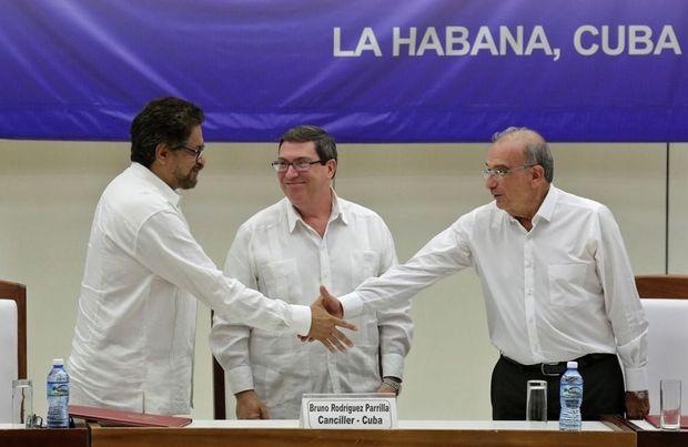Ivan Marquez, hoofdonderhandelaar van de FARC, schudt de hand van regeringsonderhandelaar Humberto de la Calle, terwijl de Cubaanse minster van Buitenlandse Zaken Bruno Rodriguez toekijkt.