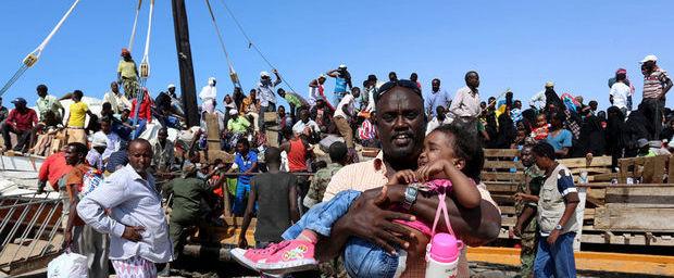 Een man draagt zijn kind een schip af. Dat arriveerde pas vol Jemenitische vluchtelingen in de haven van Bosasso in Somalië.
