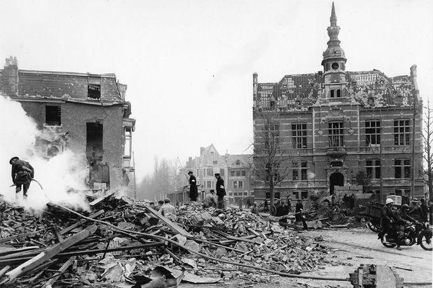 Het Mortselse Gemeenteplein na het bombardement, met centraal de uitgebrande bus en achteraan de getroffen Sint-Lutgardisschool.