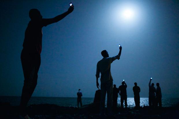 2014. Des migrants sur la côte, à Djibouti, tentent de capter un signal avec leur téléphone.