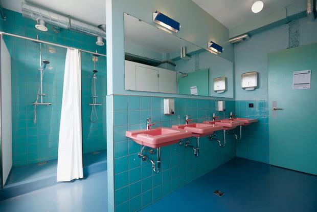 Oddsson Ho(s)tel in Reykjavik. Deze gedeelde badkamer ademt de sfeer van de jaren vijftig. Met dank aan de turquoise tegels, een pastelblauwe vloer en een rij zoetroze wastafels.