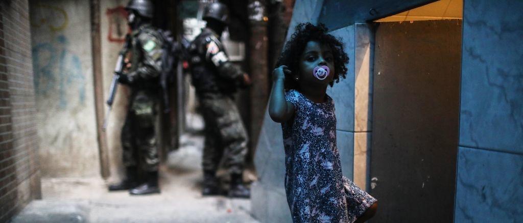 Een meisje uit de Rocinha favela in Rio de Janeiro is onderweg naar huis, terwijl achter haar enkele soldaten op patrouille zijn.