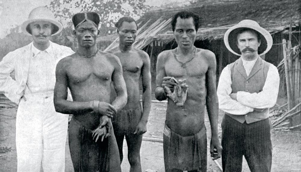 Mai 1904, au Congo. Des indigènes tiennent les mains coupées de deux travailleurs assassinés par des sentinelles. Les deux blancs sont des missionnaires baptistes, qui ont informé l'activiste britannique Edmund Morel sur les atrocités commises au temps de la récolte du caoutchouc.
