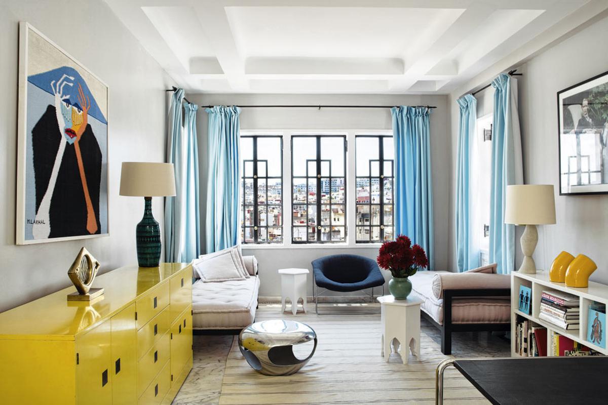 De geel gelakte kast, de felblauwe gordijnen en het modernistische meubilair geven de kamer een vrolijk karakter.