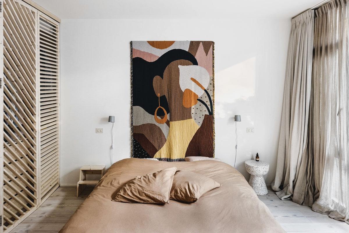 In de slaapkamer biedt een van de kleerkasten - een ontwerp van Wøti - toegang tot de badkamer. Boven het bed van Marina Bautier hangt een wandtapijt van Natalia Vico voor Slowdown Studio. De gordijnen zijn van Designs of the Time en Nathalie Van der Massen.