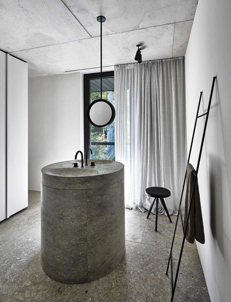 Architect Verstuyft ontwierp een ronde, gestileerde wastafel in natuursteen, het enige opvallende element in een badkamer die voor de rest achter kasten verdwijnt.