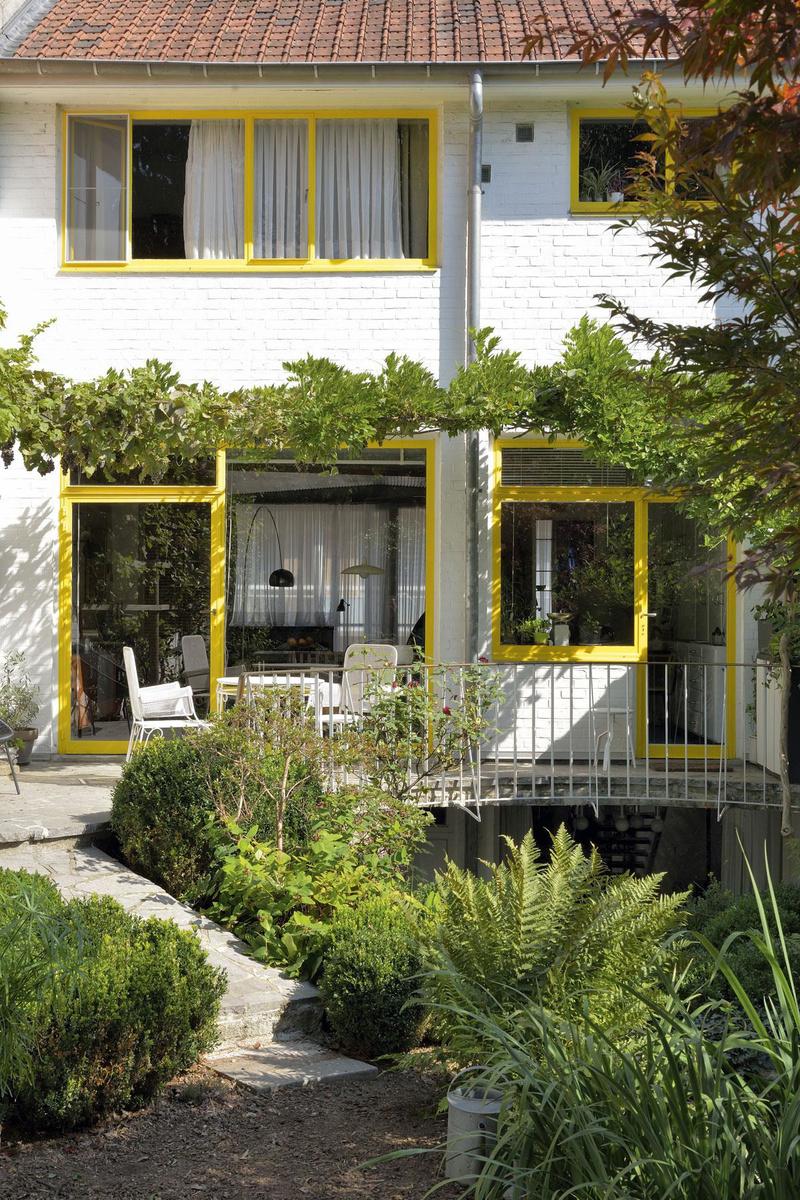 De geel geschilderde raamkozijnen zorgen voor een fris accent op de achtergevel. De tafel en stoelen op het zonneterras werden ontworpen door Jacques Dupuis.