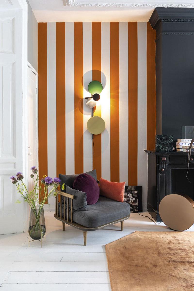 Decorateur Theo-Bert Pot schilderde zijn muur aan weerszijden van de haard in oranje strepen. Zo geeft hij extra diepte aan de kamer, zonder het evenwicht van de ruimte te verstoren.
