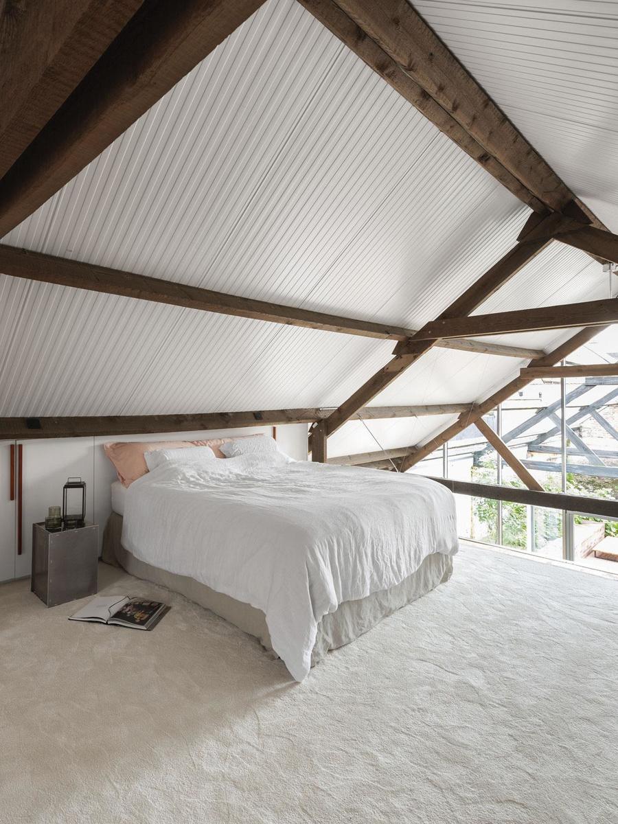Het hangargevoel blijft overeind door het golfplaten dak waaronder Ben en Eva slapen. Huis Mortier ontwierp de maatkasten achter het bed, het tapijt komt van Carpetright.
