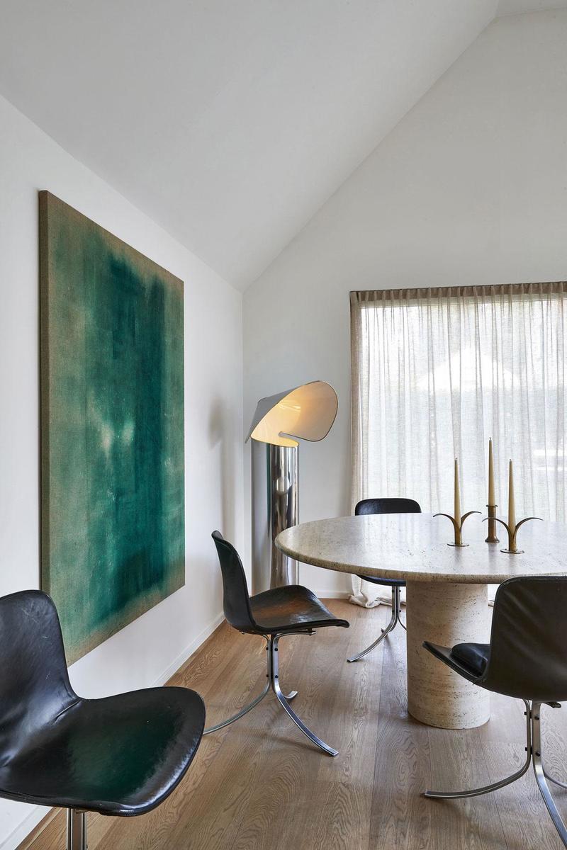 Aan de eettafel staan PK9-stoelen van Poul Kjaerholm. Het schilderij is van Dean Recoules, de kandelaars van Pierre Forsell. De lamp is de Chiara van Mario Bellini.
