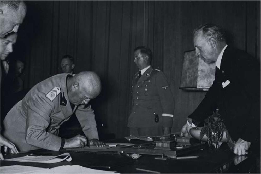 Mussolini signant les accords de Munich. A droite, Bormann et von Ribbentrop lui montrant où apposer sa signature.