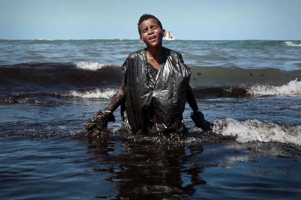 Un garçon sort de la mer en retirant le pétrole déversé sur la plage d'Itapuama située dans la ville de Cabo de Santo Agostinho, État de Pernambuco, Brésil, fin octobre 2019.