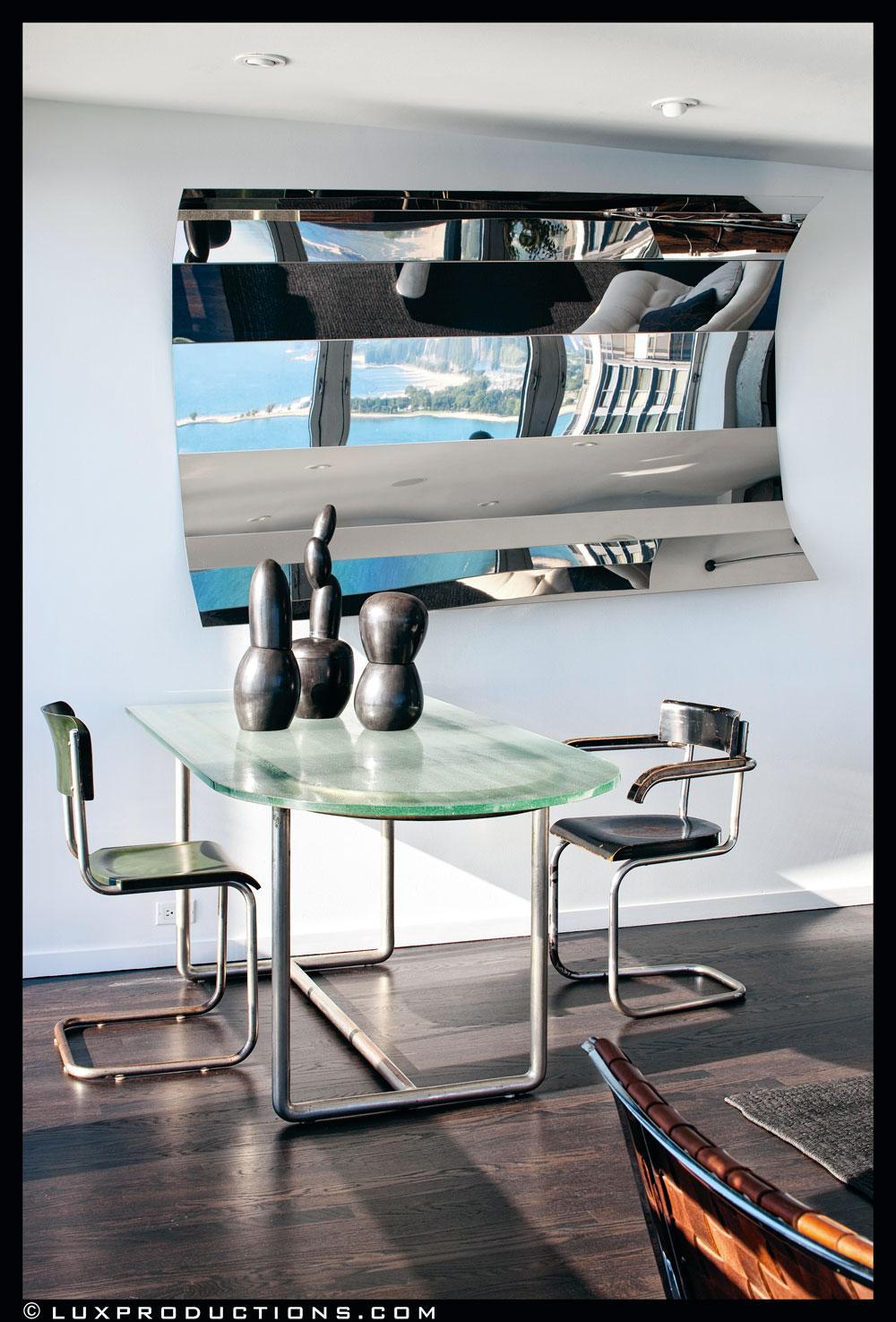 Dans le miroir en acier imaginé par Arik Levy se reflète la superbe vue sur le lac Michigan. Devant celui-ci, une table en métal et verre et des sièges de René Herbst. Les sculptures anonymes datent des années 60.