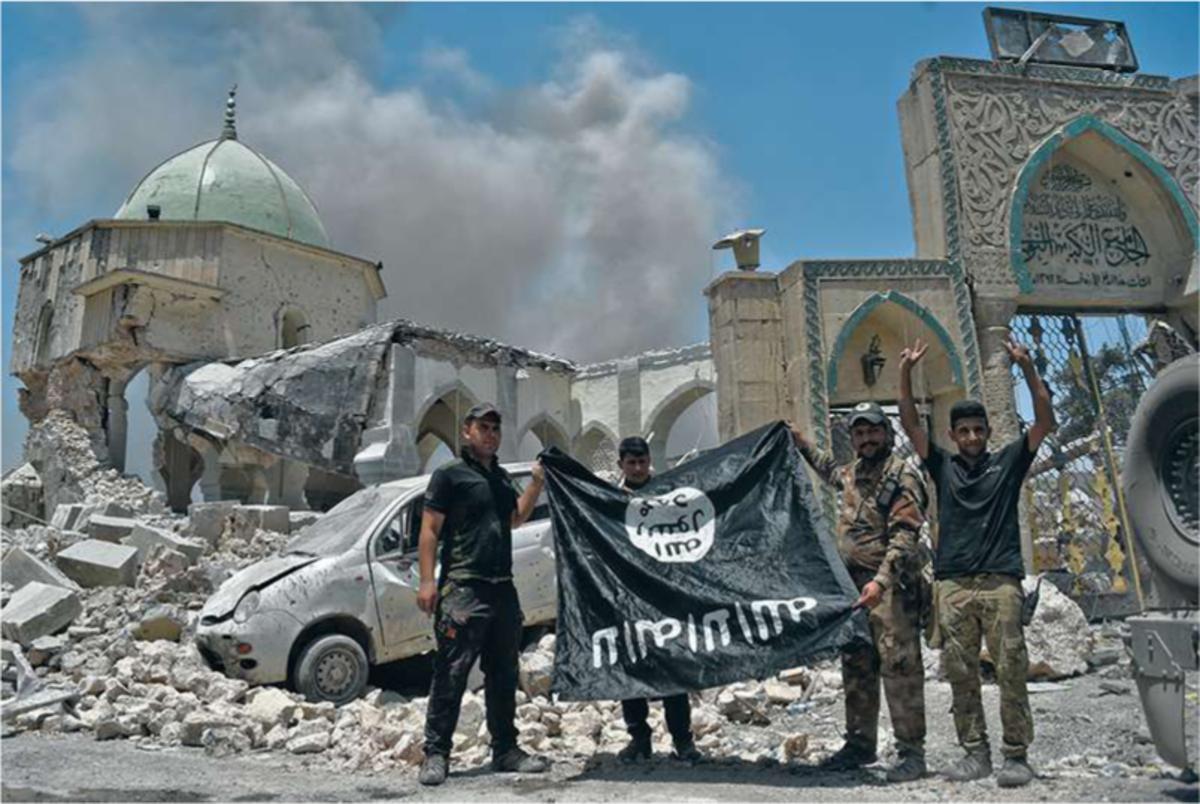 Mossoul (Irak), 30 juin 2017. Les forces spéciales irakiennes viennent de reprendre la grande mosquée Al-Nouri au groupe État islamique. Devant la mosquée en ruine, les soldats symbolisent la chute de l'EI en brandissant son drapeau avec la tête en bas.