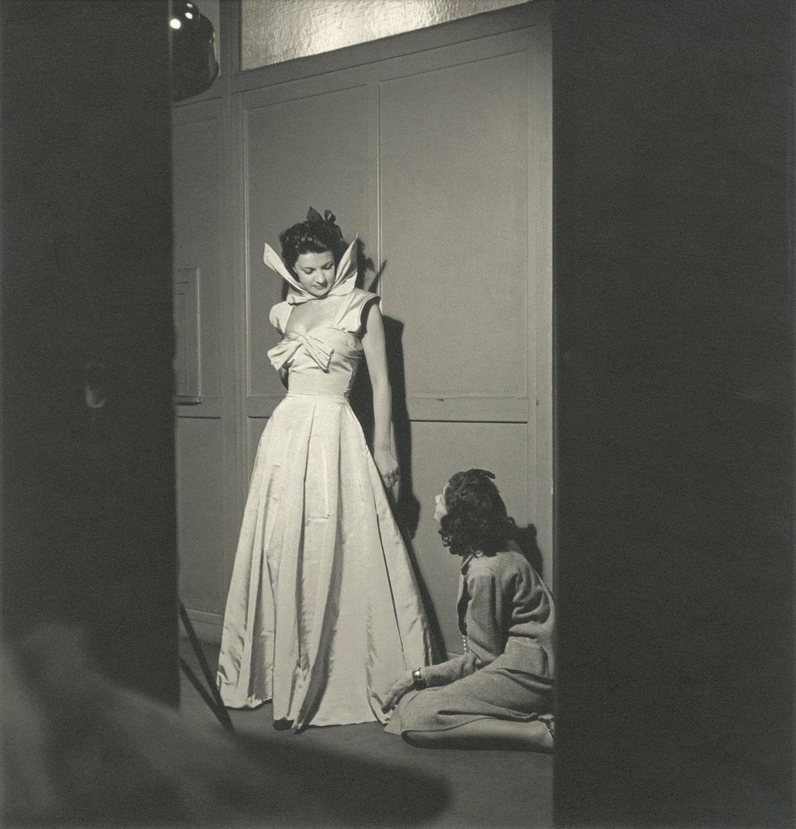 En 1939, un portrait de Gabrielle Chanel agenouillée devant un mannequin portant une longue robe de la griffe.