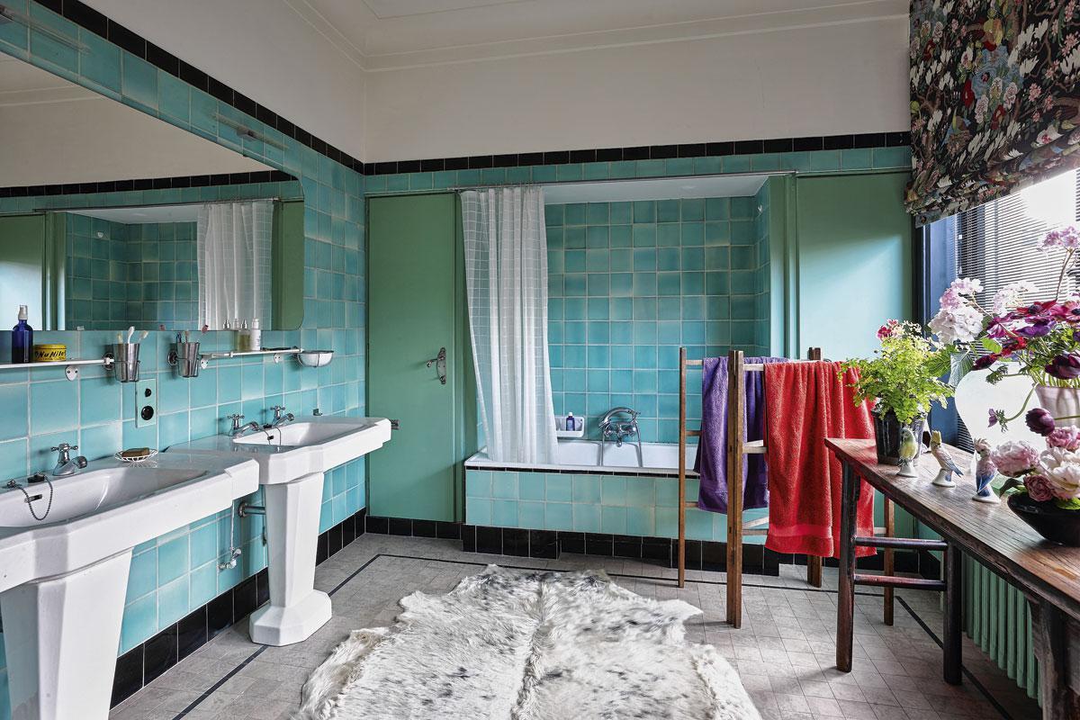 La salle de bains des années 40, avec son carrelage vert et ses lavabos typiques, est restée dans son jus. Seul le store fleuri est neuf et apporte du contraste et de la chaleur à la pièce.