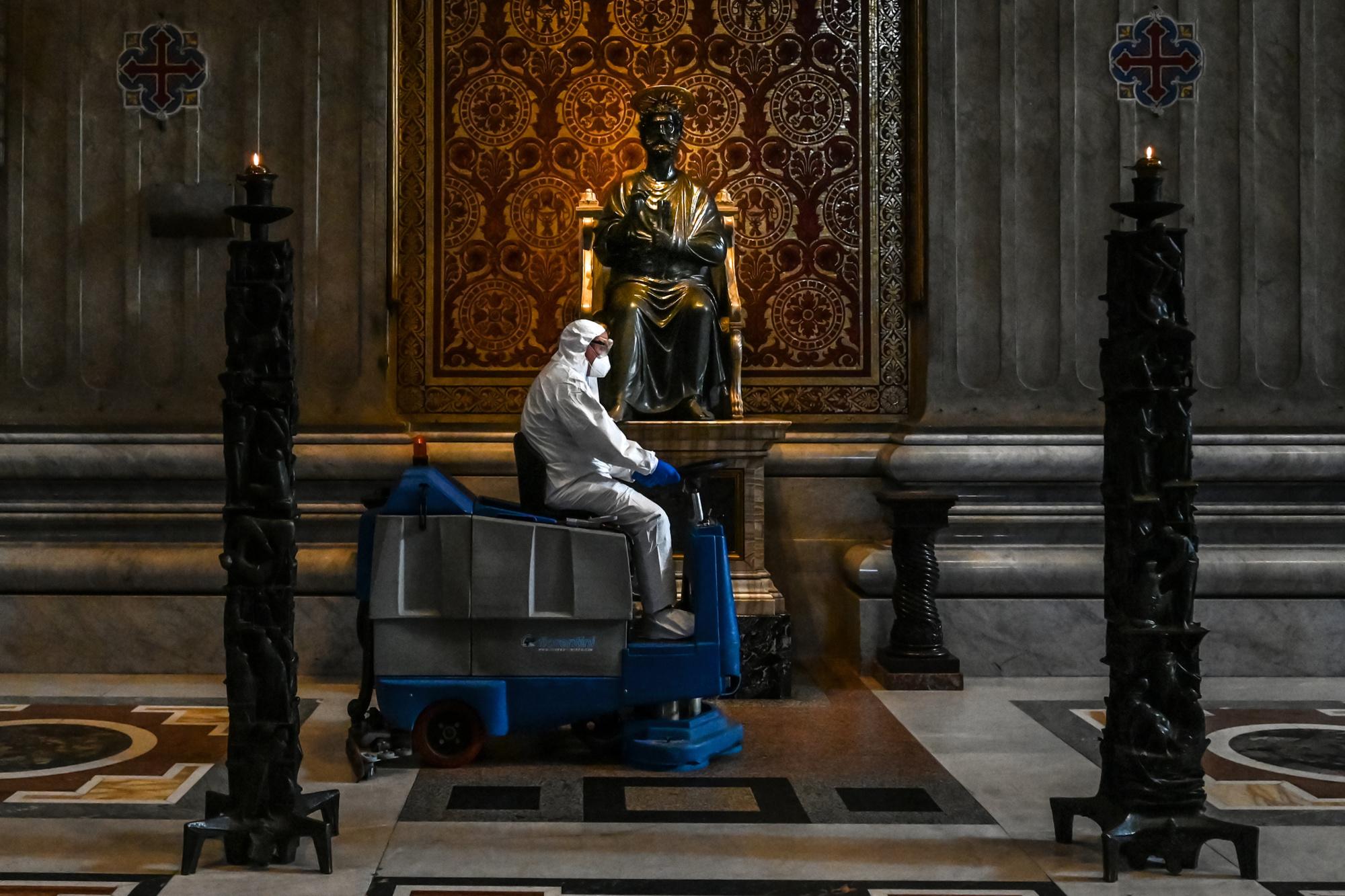 Un homme portant une combinaison de protection et un masque conduit une machine de nettoyage des sols devant une statue de Saint-Pierre lors de l'assainissement de la basilique Saint-Pierre au Vatican le 15 mai 2020