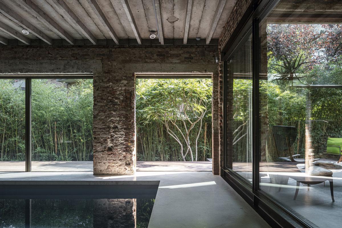 Une robuste fenêtre en acier donne sur la piscine intérieure. Dans le jardin, de grandes tiges de bambou bloquent la vue, car l'ancien gymnase est situé au milieu d'une cour intérieure, entourée d'immeubles à appartements.