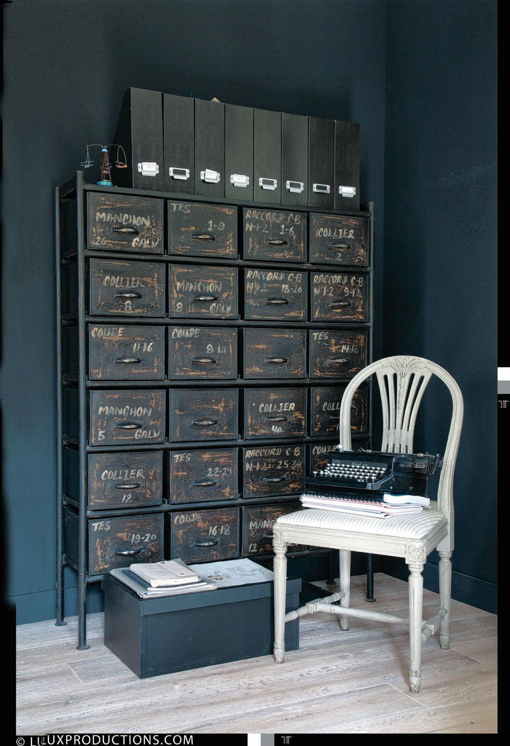 Dans son bureau aux murs noirs, un meuble industriel lui sert de rangement.