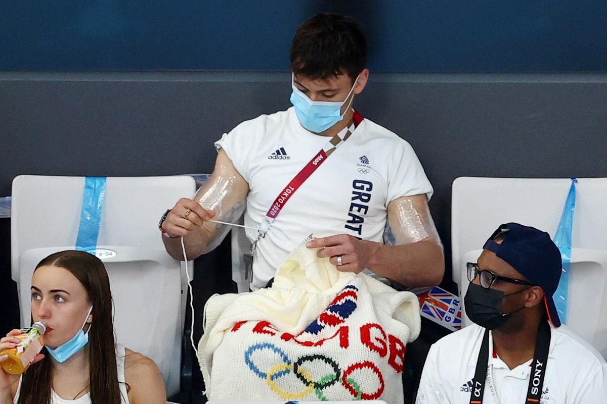 Tom Daley en train de tricoter un pull garni des anneaux entrelacés, durant les JO 2020 de Tokyo.