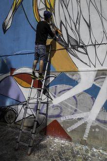Straatartiest Dzia spuit zijn kunstwerk op de muur in de Lange Schipstraat.