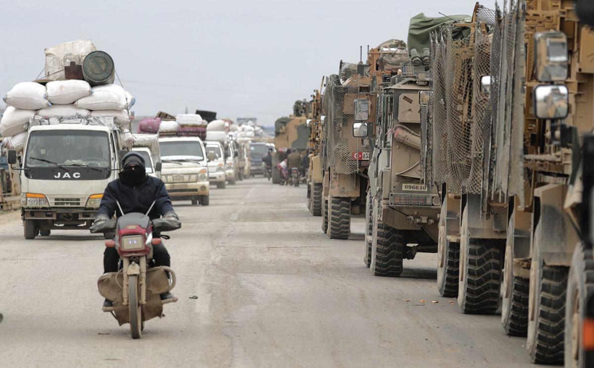 Un convoi de déplacés croise des véhicules de la force d'occupation turque à Hazano, près d'Idlib.