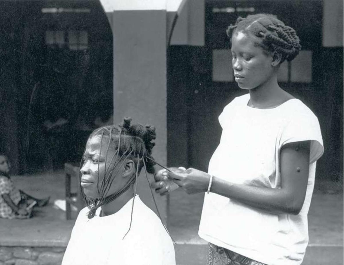 Photo prise dans les années 1950 montrant une femme congolaise en coiffant une autre.