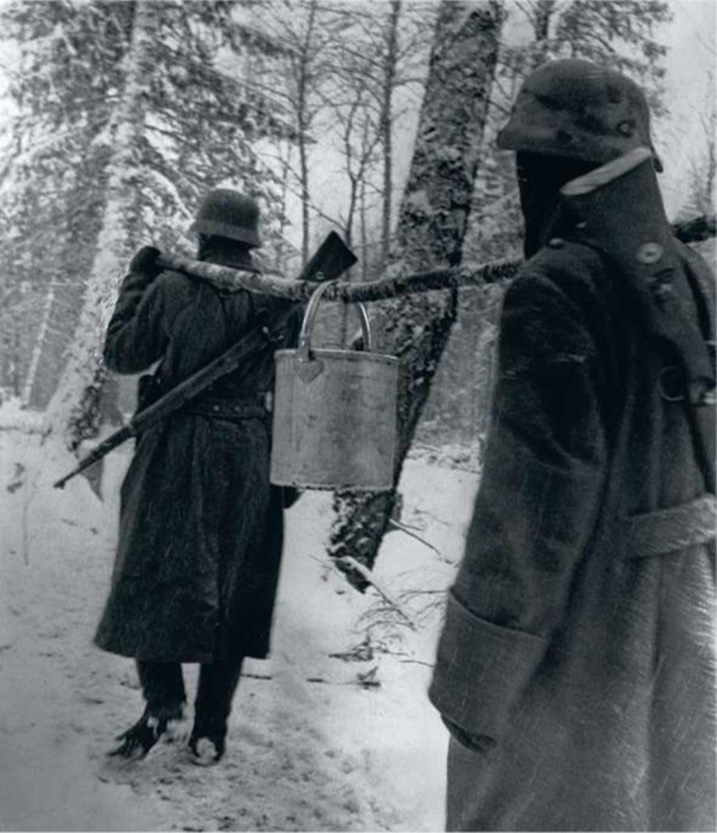 Sur le front de l'Est, dans une forêt russe enneigée, des soldats transportent un seau d'eau.