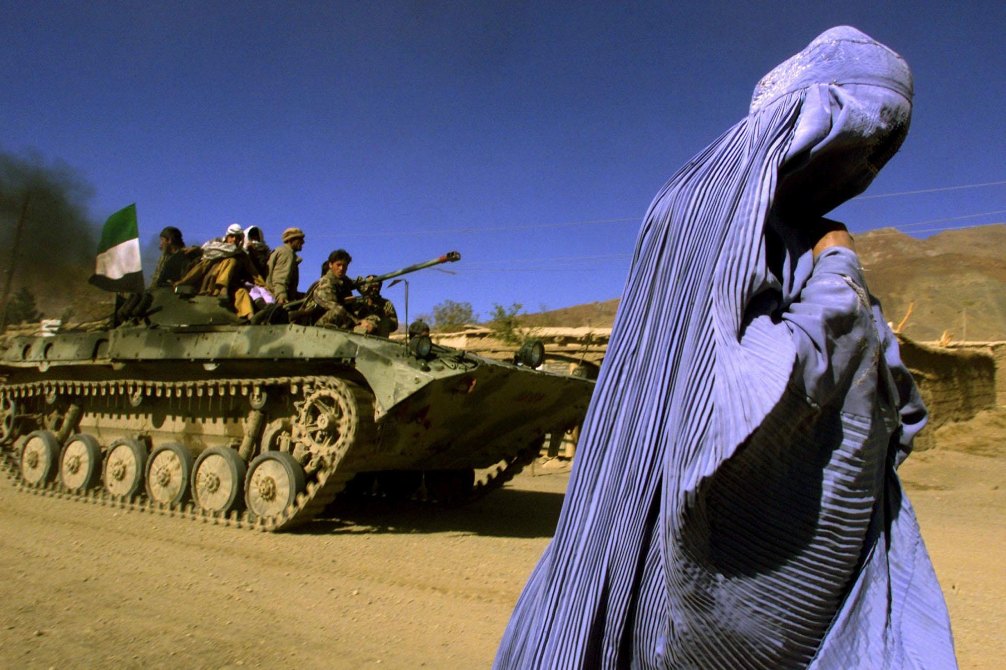 4 novembre 2001 : une Afghane portant une burqa traditionnelle marche sur le bord d'une route alors qu'un véhicule blindé de l'Alliance du Nord, transportant des combattants et le drapeau afghan, se dirige vers une nouvelle position dans la périphérie de Jabal us Seraj, à environ 60 km au nord de la capitale afghane Kaboul.