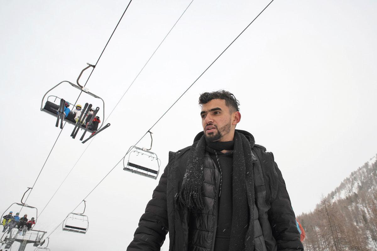Karim, 23 ans, réfugié afghan, passe sous un télésiège de Montgenèvre. Les skieurs observent, médusés, le cortège de migrants qui se faufilent au milieu des pistes.