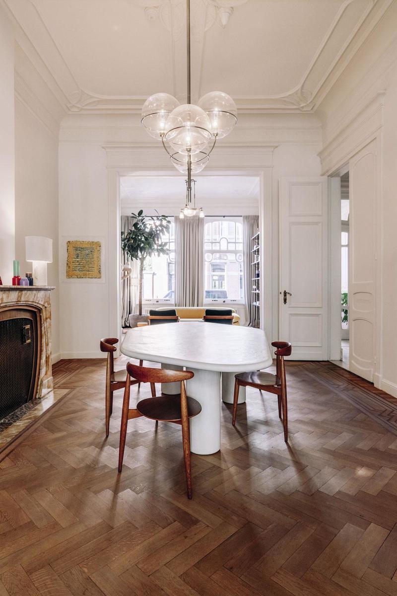 Rond de organische eettafel van Armand & Francine staan Heart-stoelen van de Deense ontwerper Hans Wegner. De originele art-nouveauluchter vonden ze te bombastisch. In de plaats kwam een Lyndon-hanglamp van Oluce: een ontwerp van Vico Magistretti uit 1977. Het parket is authentiek.