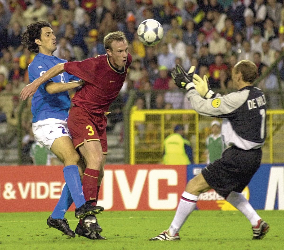 Filip De Wilde staat klaar om een kopbal van Joos Valgaeren, die wordt opgejaagd door de Italiaan Marco Delvecchio, op te vangen.